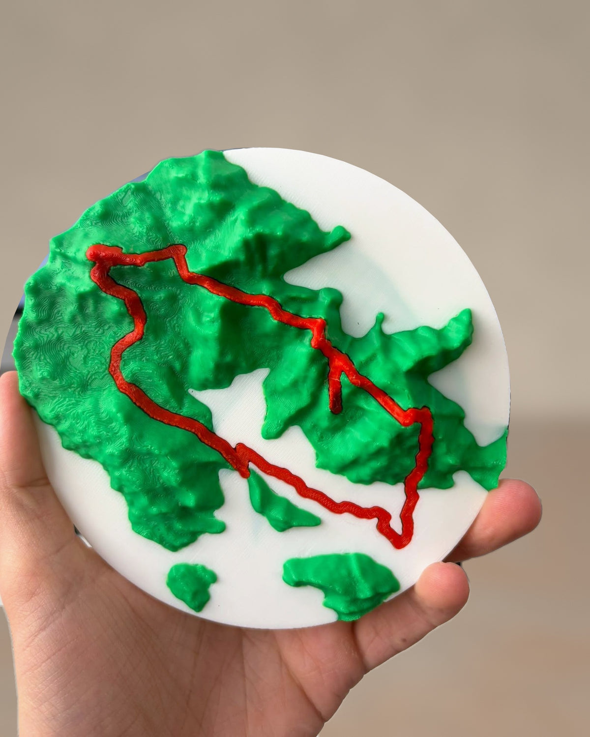The terrain disc lifted off its mount and held in one hand, route in red across green ridges